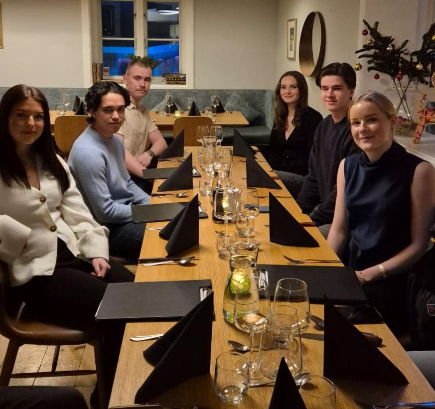 flera unga människor sitter längs ett bord